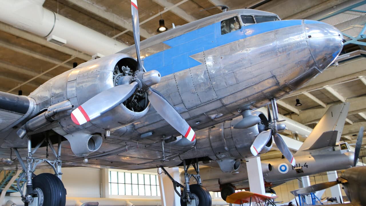 Suuri hopeanvärinen DC-3-lentokone museon näyttelyssä. Metallisissa potkureissa on kolme lapaa.