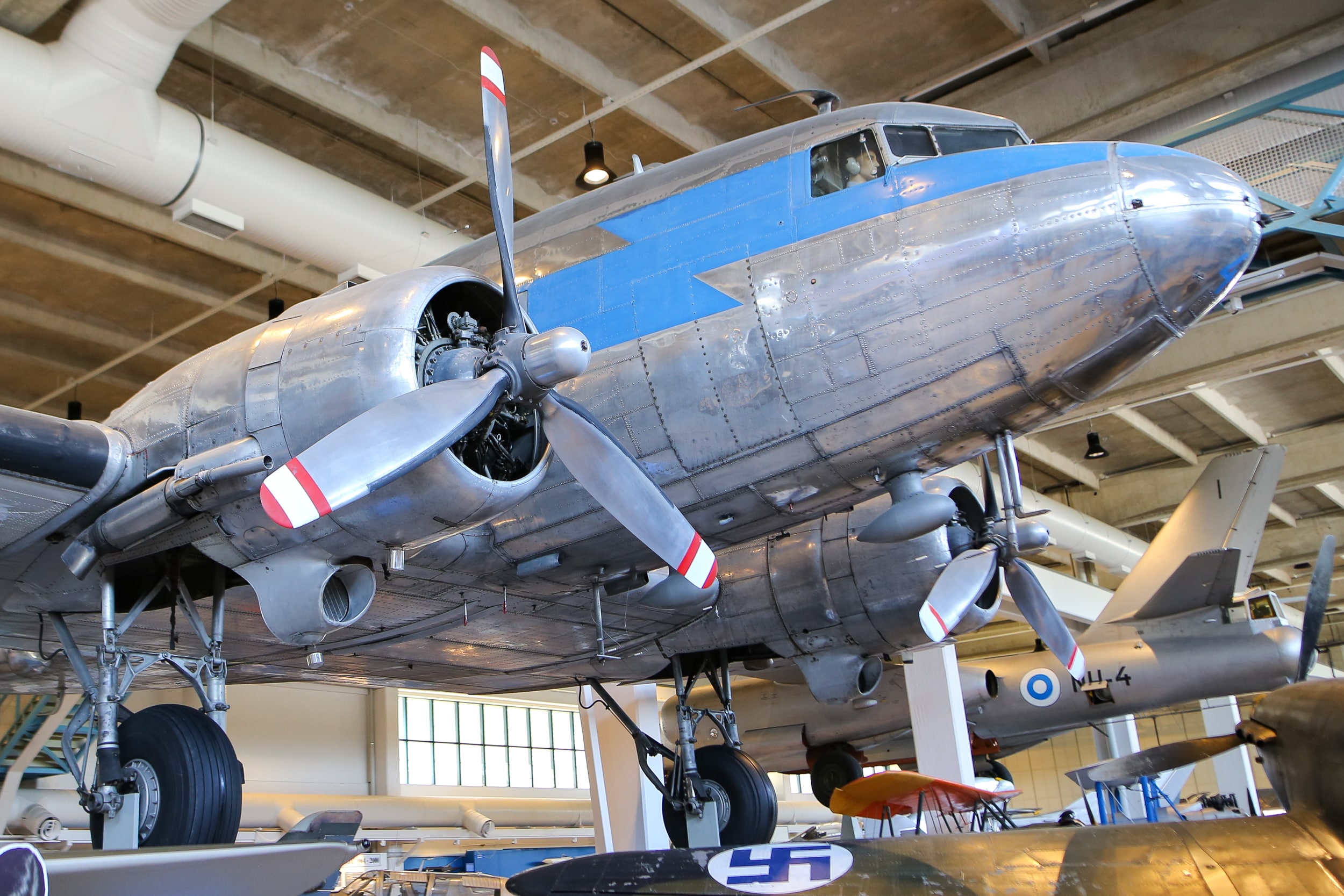 Suuri hopeanvärinen DC-3-lentokone museon näyttelyssä. Metallisissa potkureissa on kolme lapaa.