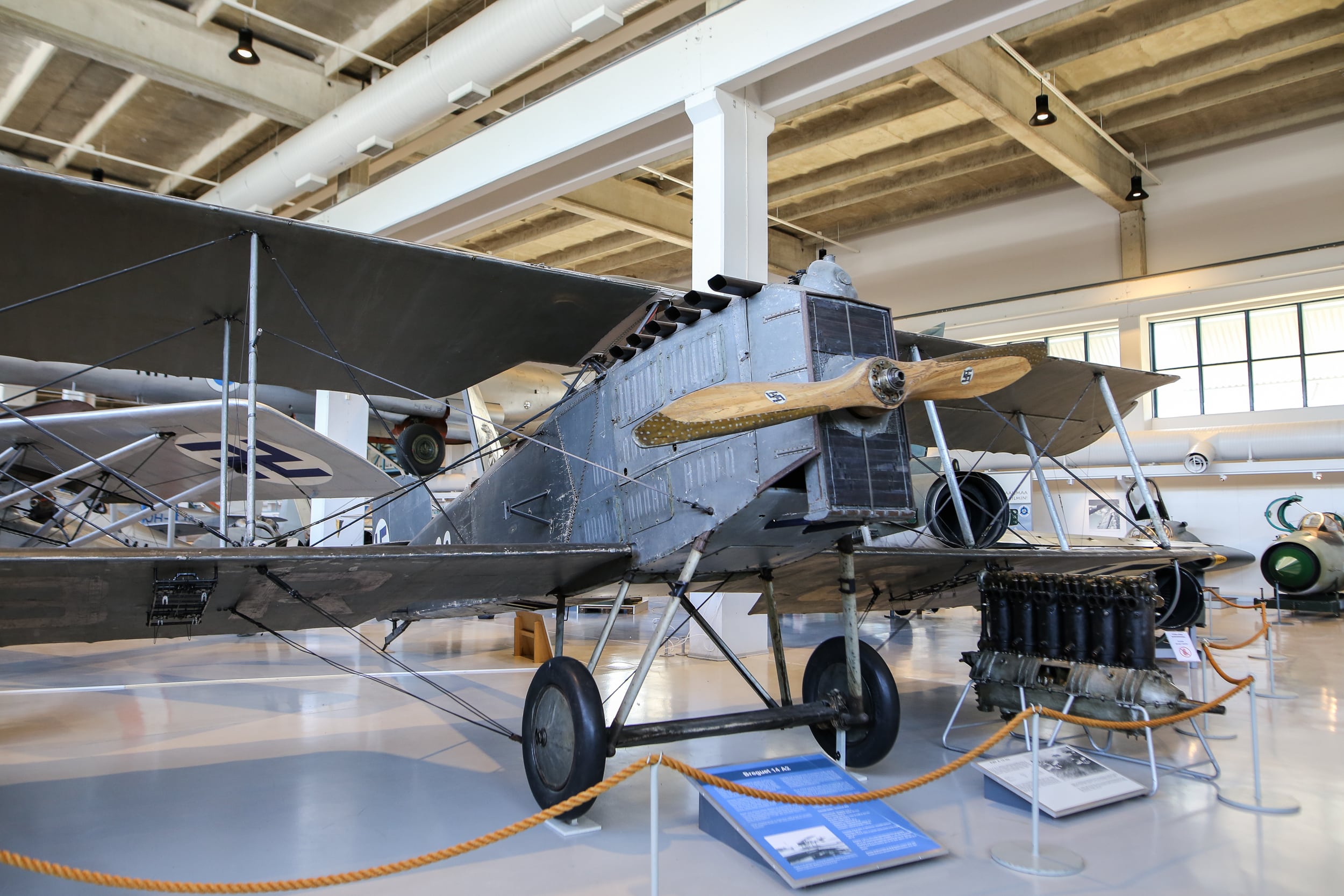 Kaksitasoinen, harmaa, puupotkurilla varustettu Breguet-lentokone näyttelyhallissa.