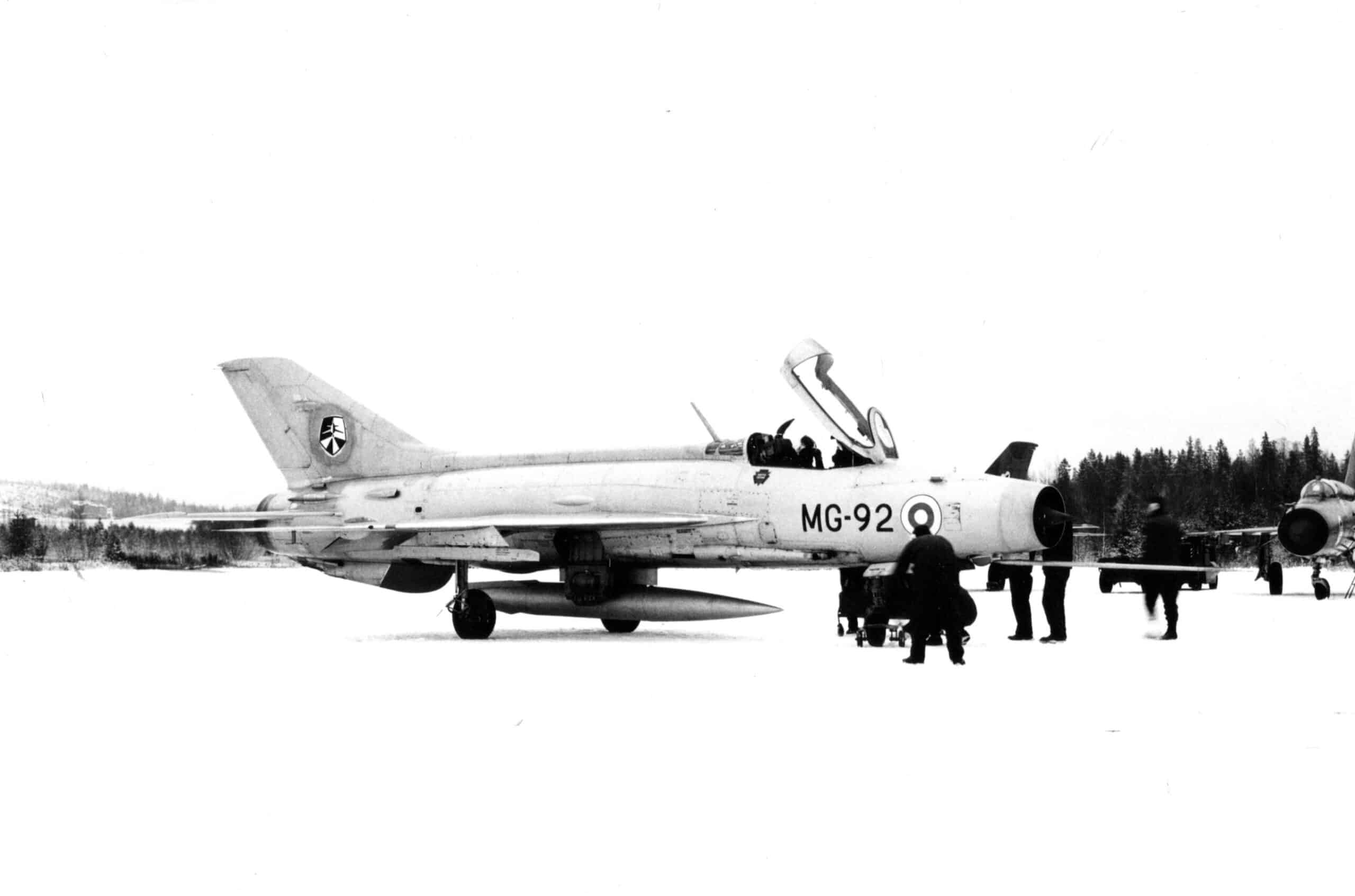 MiG-21 lumisella kiitoradalla. Ohjaamon kuomu on auki. Ympärillä on ihmisiä.