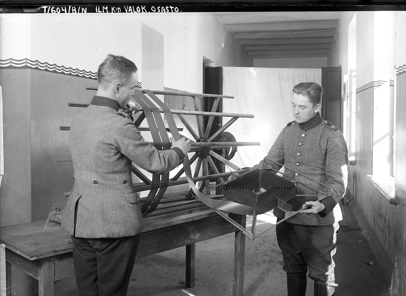 Vanha kuva, jossa kaksi miestä käsittelee pitkää valokuvanegatiivia.